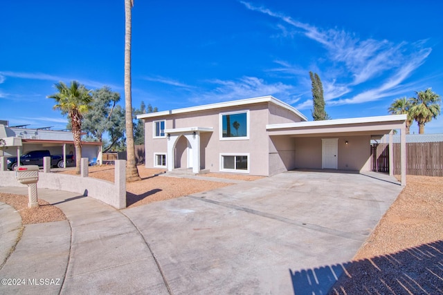view of front facade featuring stucco siding, driveway, a carport, and fence