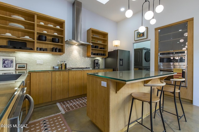 kitchen featuring brown cabinets, open shelves, backsplash, appliances with stainless steel finishes, and wall chimney exhaust hood