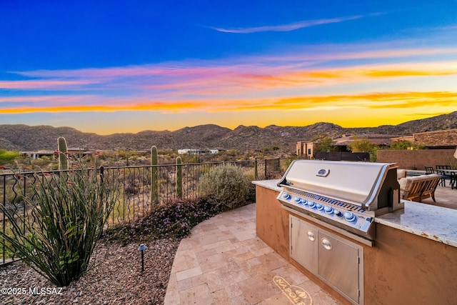 14623 N Shaded Stone Pl, Oro Valley, AZ 85755 - patio terrace at dusk featuring a mountain view, fence, exterior kitchen, and a grill