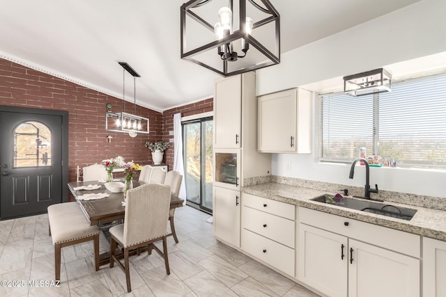 kitchen with vaulted ceiling, a sink, brick wall, white cabinets, and an inviting chandelier