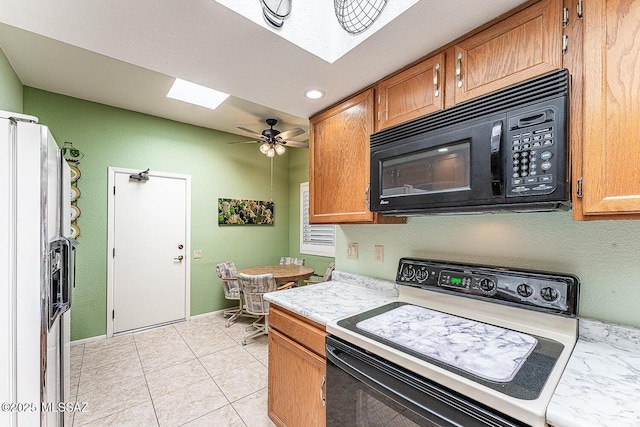 kitchen featuring light countertops, refrigerator with ice dispenser, a skylight, black microwave, and electric range oven
