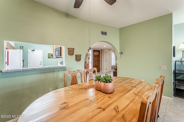 tiled dining room featuring arched walkways, a high ceiling, visible vents, and a ceiling fan