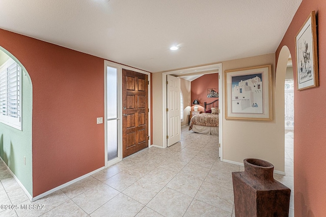 foyer entrance with light tile patterned flooring, arched walkways, and baseboards