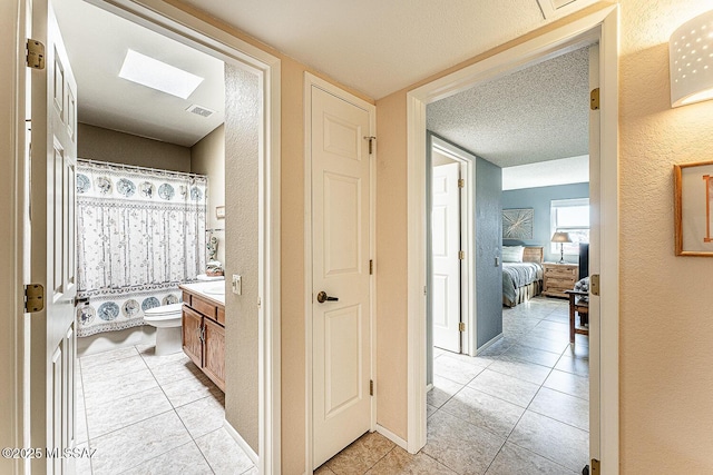 corridor featuring light tile patterned flooring, a textured ceiling, visible vents, and a skylight
