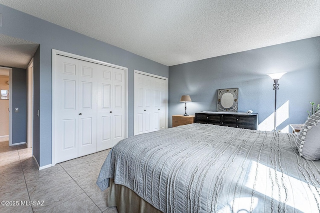 tiled bedroom with baseboards, a textured ceiling, and two closets