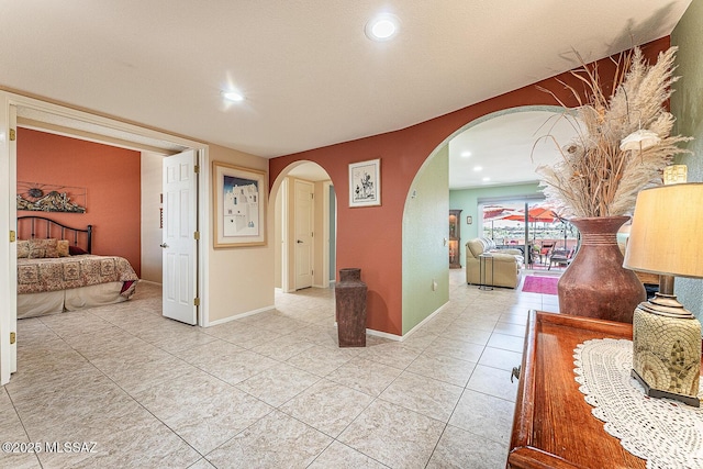 hallway with arched walkways, baseboards, recessed lighting, and light tile patterned floors