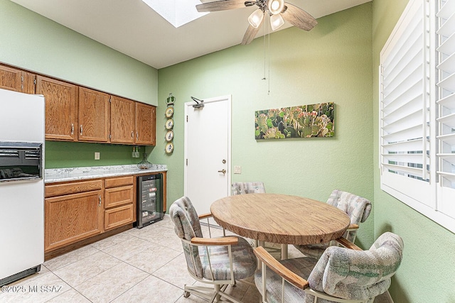 kitchen featuring light countertops, light tile patterned flooring, beverage cooler, freestanding refrigerator, and brown cabinetry