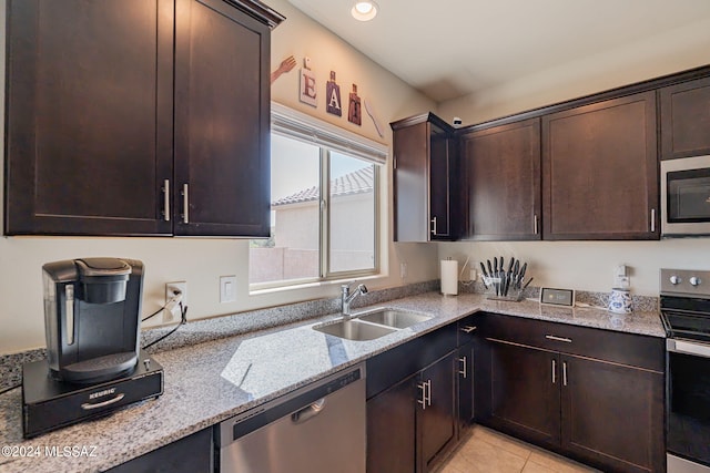 kitchen featuring light stone countertops, stainless steel appliances, dark brown cabinetry, a sink, and light tile patterned floors