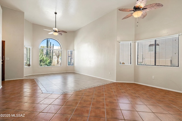 empty room featuring baseboards, high vaulted ceiling, tile patterned flooring, and a ceiling fan