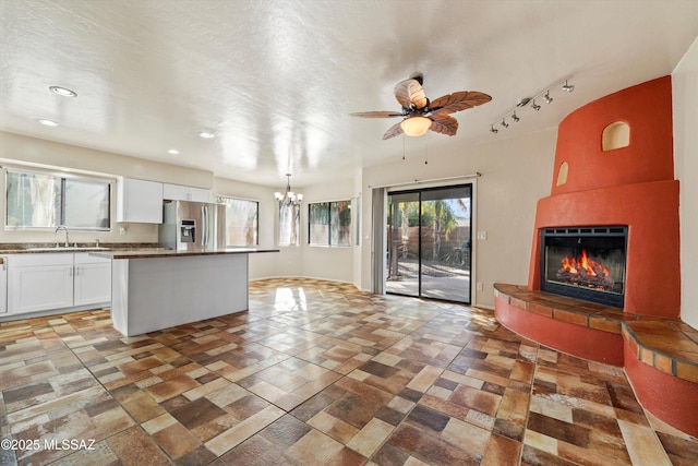 kitchen with stainless steel fridge, ceiling fan with notable chandelier, a sink, white cabinets, and a fireplace