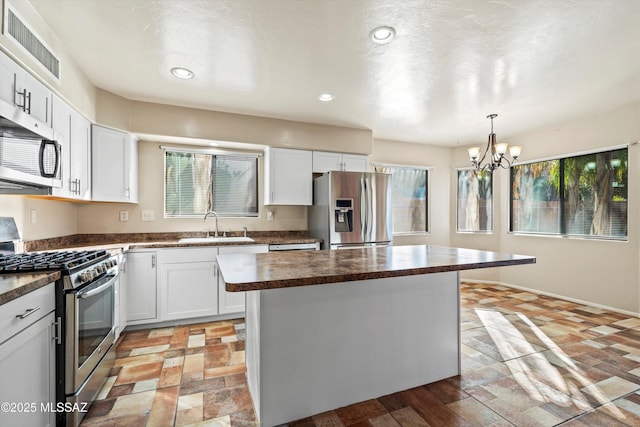 kitchen with a sink, a chandelier, appliances with stainless steel finishes, dark countertops, and white cabinets