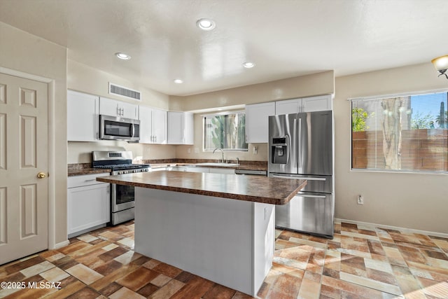 kitchen featuring white cabinetry, stainless steel appliances, a kitchen island, a sink, and visible vents