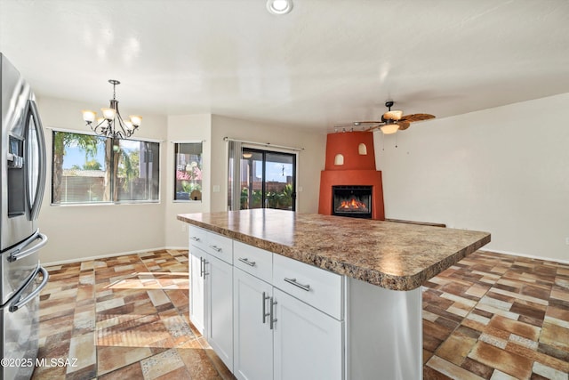 kitchen featuring a large fireplace, white cabinets, stainless steel fridge, decorative light fixtures, and ceiling fan with notable chandelier