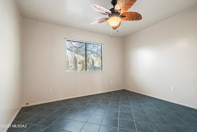 spare room with a ceiling fan, dark tile patterned floors, and baseboards