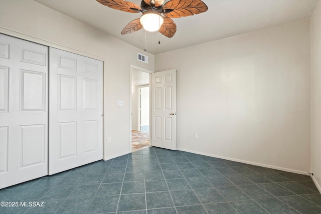 unfurnished bedroom with a closet, a ceiling fan, baseboards, visible vents, and dark tile patterned flooring