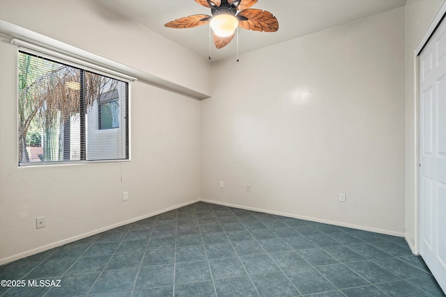 spare room featuring baseboards, ceiling fan, and dark tile patterned floors