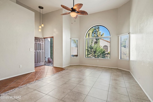 tiled empty room with baseboards, ceiling fan, and a towering ceiling