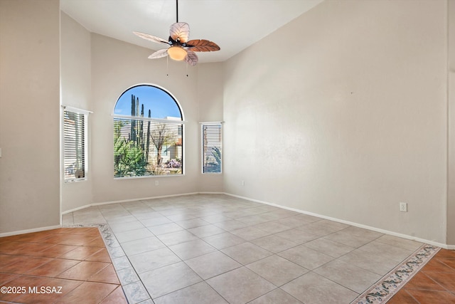 empty room with baseboards, a ceiling fan, a high ceiling, and light tile patterned floors