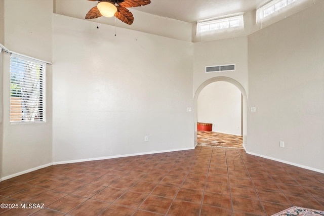 unfurnished room with arched walkways, a towering ceiling, visible vents, and a ceiling fan