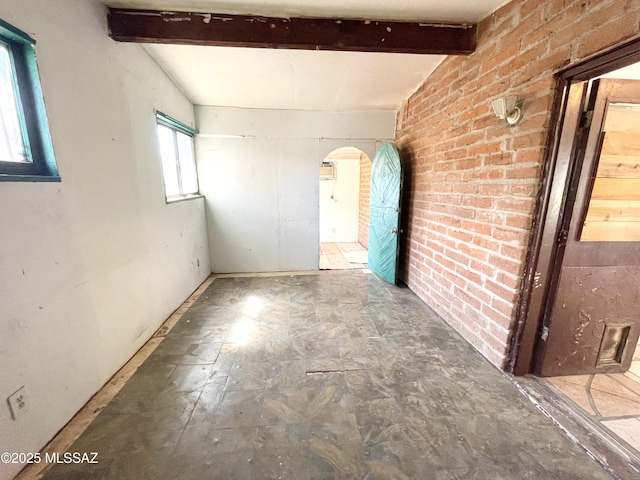 spare room featuring arched walkways, lofted ceiling with beams, and brick wall