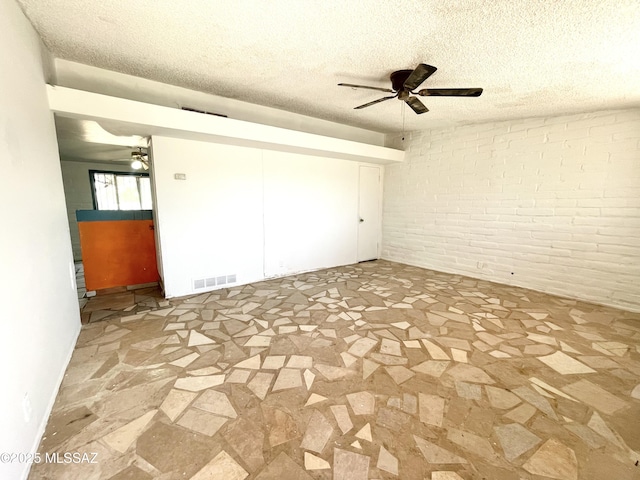 empty room featuring a ceiling fan, stone finish floor, brick wall, and visible vents