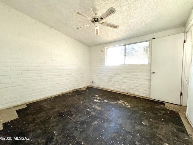 spare room featuring a textured ceiling, lofted ceiling, brick wall, and a ceiling fan