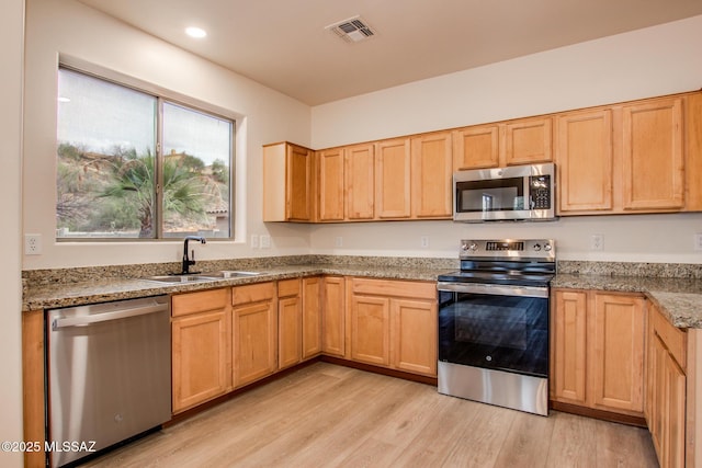 kitchen with light wood-type flooring, visible vents, a sink, light stone counters, and stainless steel appliances