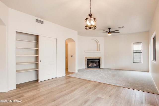 unfurnished living room with light wood finished floors, visible vents, ceiling fan with notable chandelier, a fireplace, and arched walkways