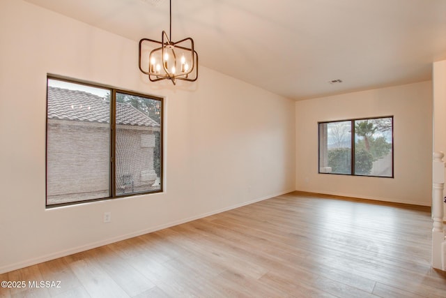 spare room featuring an inviting chandelier, baseboards, visible vents, and light wood-type flooring