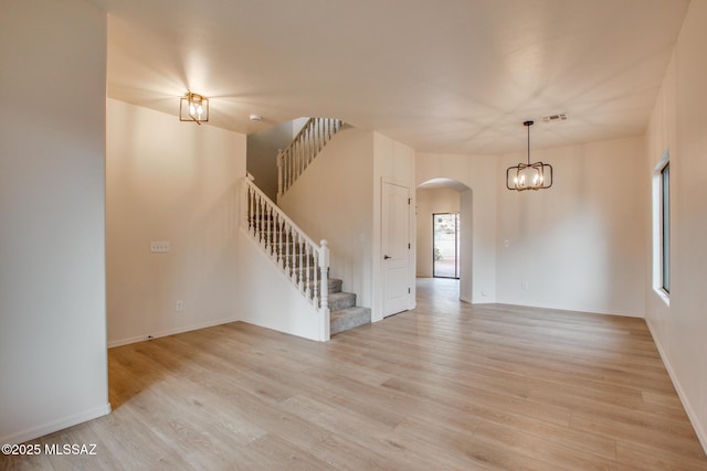 empty room featuring stairway, visible vents, light wood-style flooring, arched walkways, and a chandelier