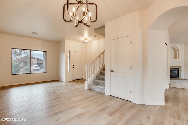 entrance foyer featuring arched walkways, light wood-style floors, a chandelier, and stairs