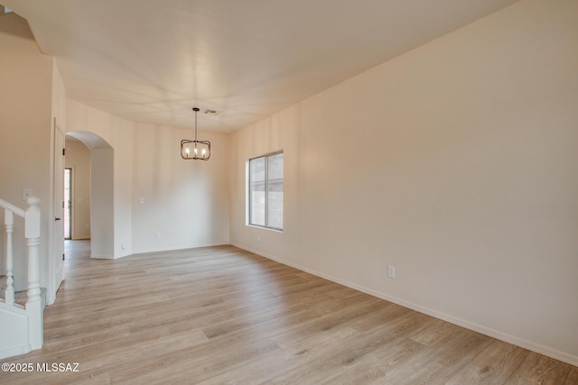 spare room with arched walkways, stairway, an inviting chandelier, and light wood-style floors