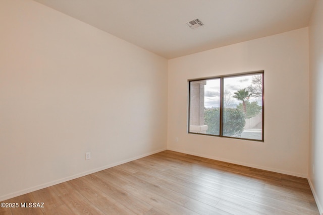 spare room featuring light wood-type flooring, visible vents, and baseboards