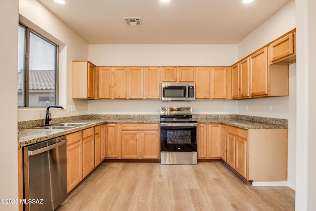 kitchen with light brown cabinets, light stone countertops, light wood-type flooring, stainless steel appliances, and a sink