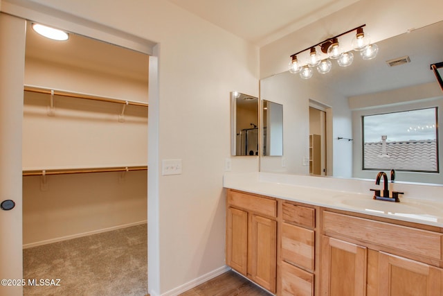 full bath with visible vents, vanity, a walk in closet, and baseboards