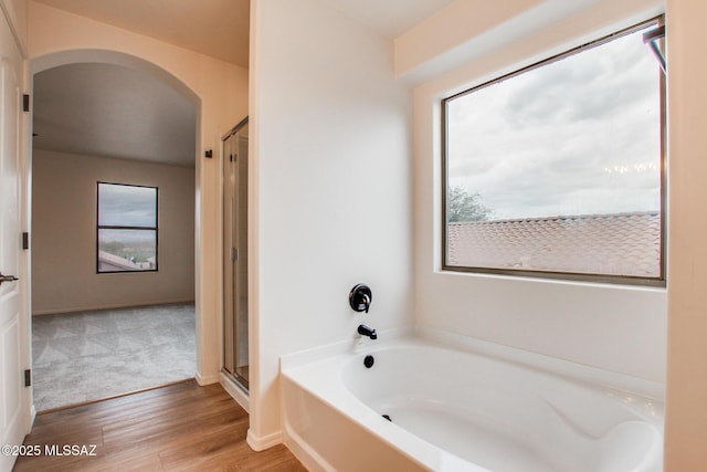 bathroom featuring a shower stall, baseboards, a garden tub, and wood finished floors