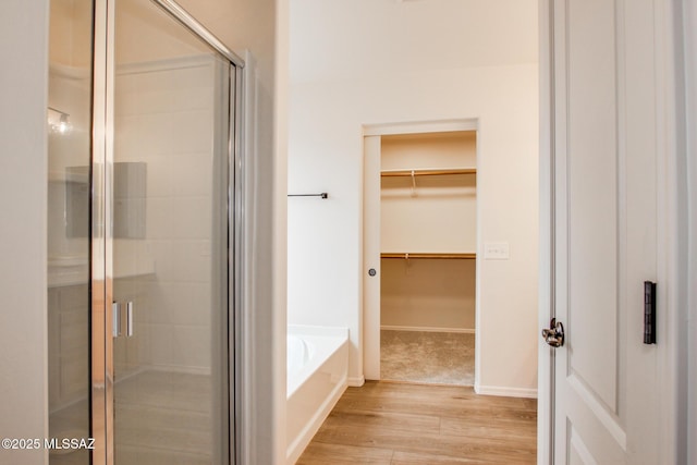 bathroom featuring a walk in closet, a stall shower, wood finished floors, baseboards, and a bath