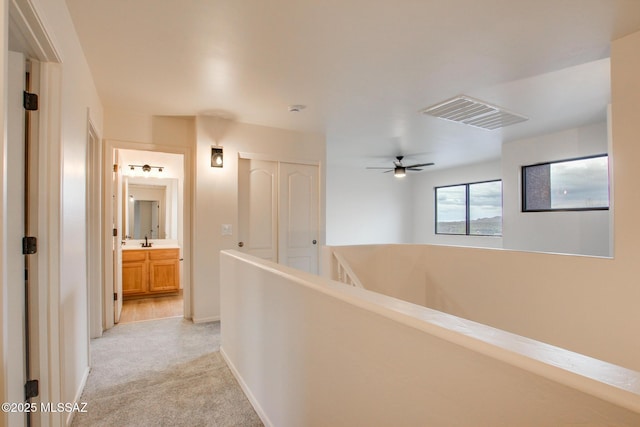corridor with baseboards, visible vents, a sink, light carpet, and an upstairs landing