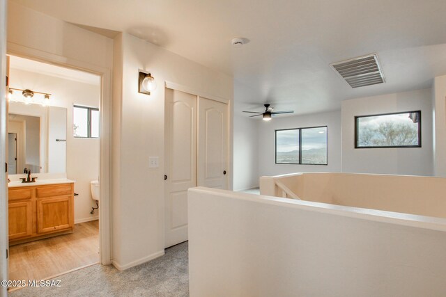 hallway featuring a sink, visible vents, baseboards, and light colored carpet