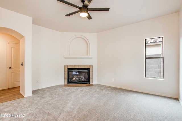 unfurnished living room with a ceiling fan, baseboards, carpet floors, a fireplace, and arched walkways