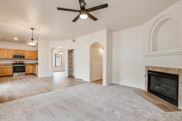 unfurnished living room with visible vents, light carpet, a ceiling fan, arched walkways, and a fireplace