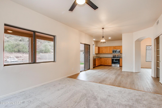 kitchen featuring a ceiling fan, arched walkways, appliances with stainless steel finishes, light colored carpet, and hanging light fixtures
