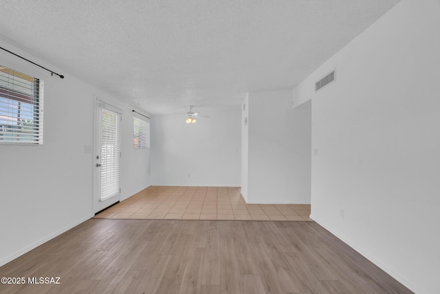 empty room with baseboards, a textured ceiling, a ceiling fan, visible vents, and wood finished floors