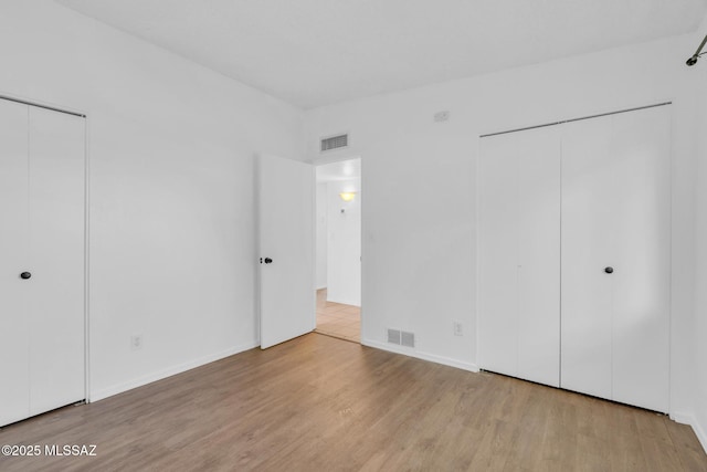 unfurnished bedroom with wood finished floors, baseboards, a closet, and visible vents