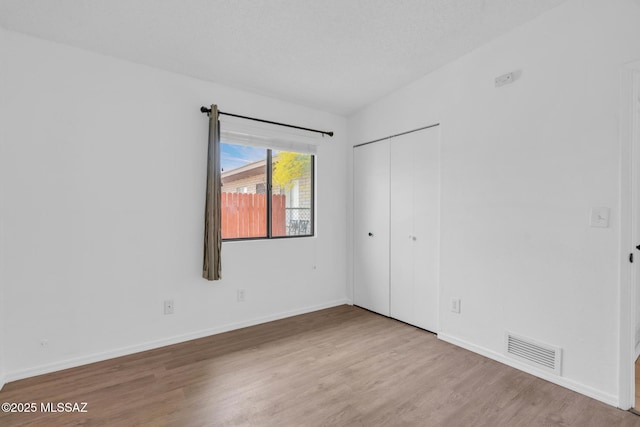 unfurnished bedroom with visible vents, baseboards, a closet, and wood finished floors