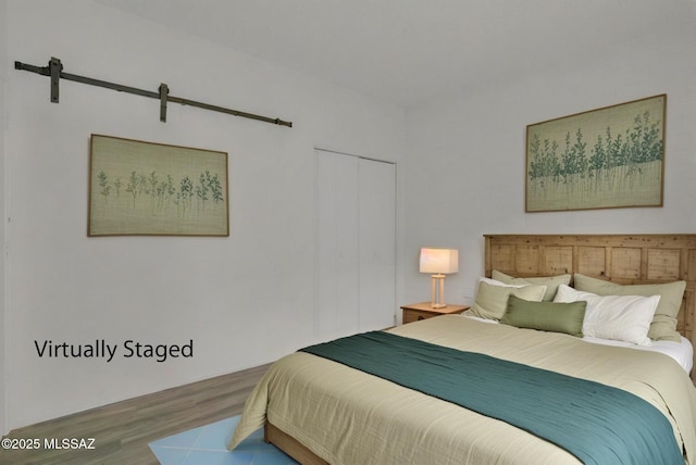 bedroom with a barn door, a closet, and wood finished floors