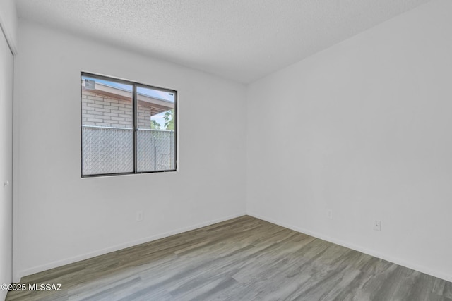 spare room featuring a textured ceiling, wood finished floors, and baseboards