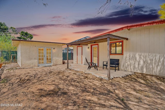 back of house at dusk featuring a patio area, french doors, and fence