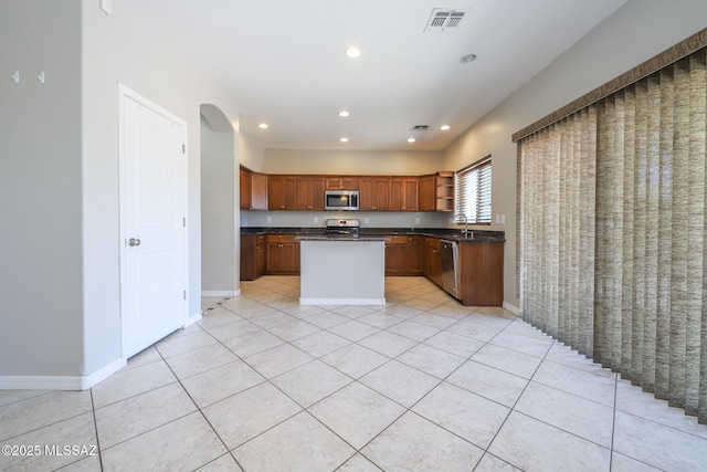 kitchen with dark countertops, open shelves, light tile patterned floors, appliances with stainless steel finishes, and a kitchen island