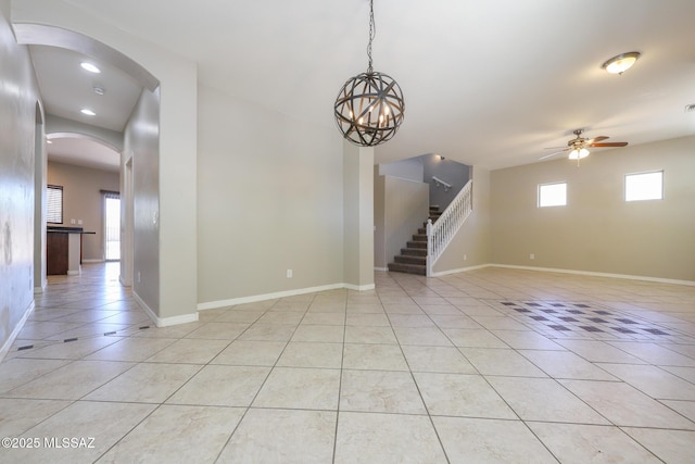 empty room with a ceiling fan, light tile patterned flooring, arched walkways, baseboards, and stairs